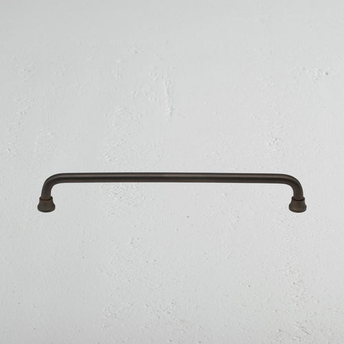 Medium bronze Sycamore Furniture Handle mounted horizontally on a textured white wall.