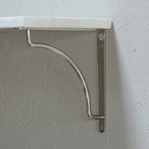 Kilburn Shelf Bracket Medium in polished nickel, with a curved design, mounted on a white textured wall.