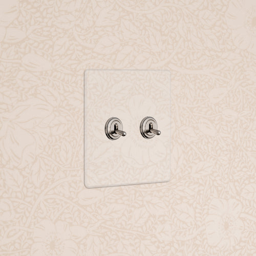Kew 2G Toggle Switch in clear polished nickel with two toggles on a white wall plate against beige floral wallpaper.