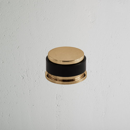 Seymour Door Stop in antique brass finish, mounted on a white textured wall.
